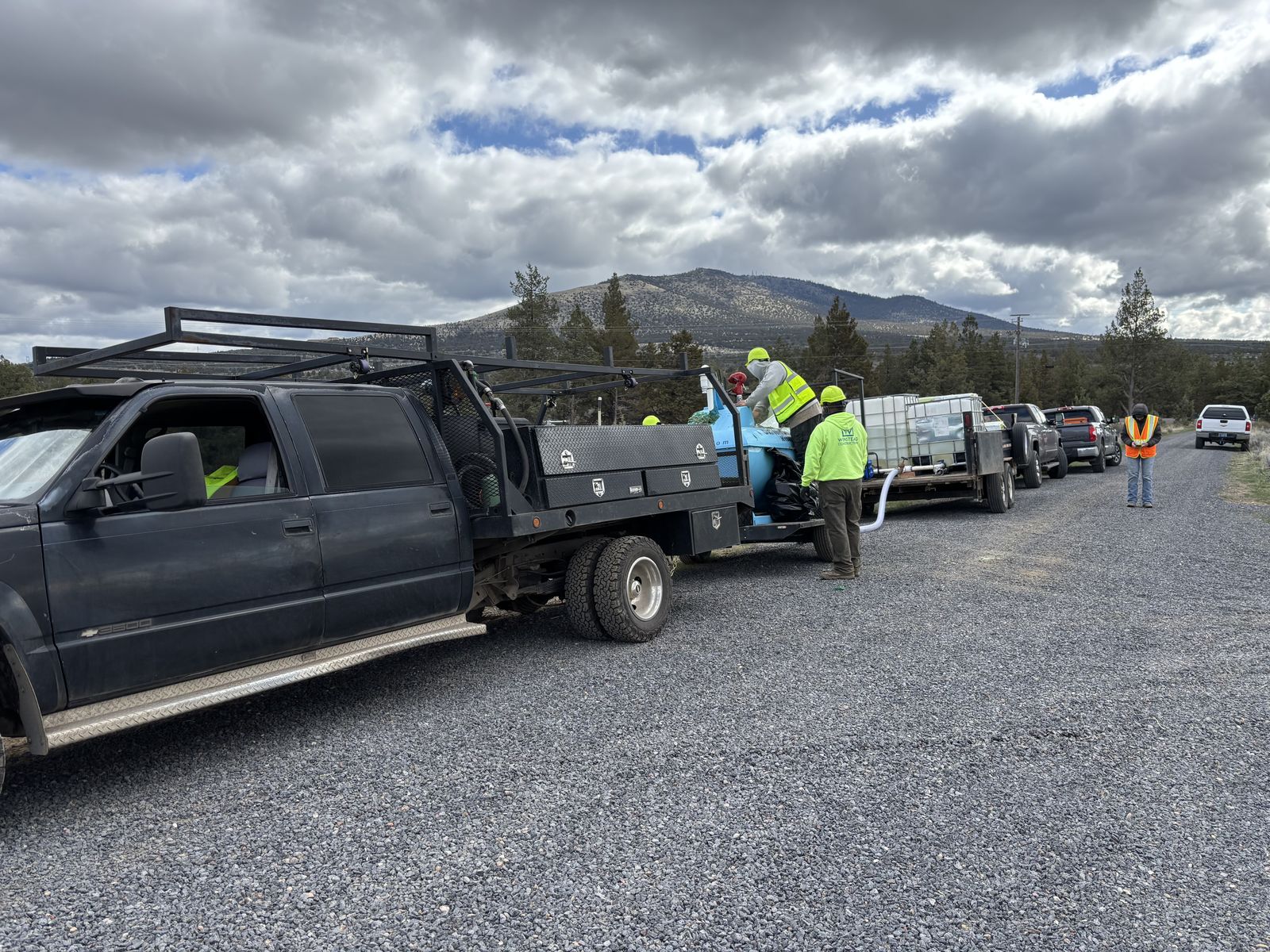 Workers in safety gear load equipment into trucks lined up on a road